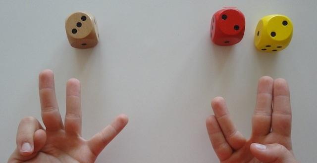 photo : à gauche : un dé avec un 3 et une main avec 3 doigts levés ; à droite : 2 dés avec un 2 et un 2 et une main avec 2*2 doigts levés (annulaire et auriculaire collés l'un à l'autre, majeur et index collés l'un à l'autre) 