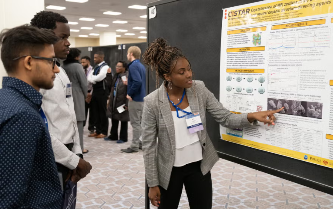 Une jeune femme présente un poster en marge d'une conférence scientifique.